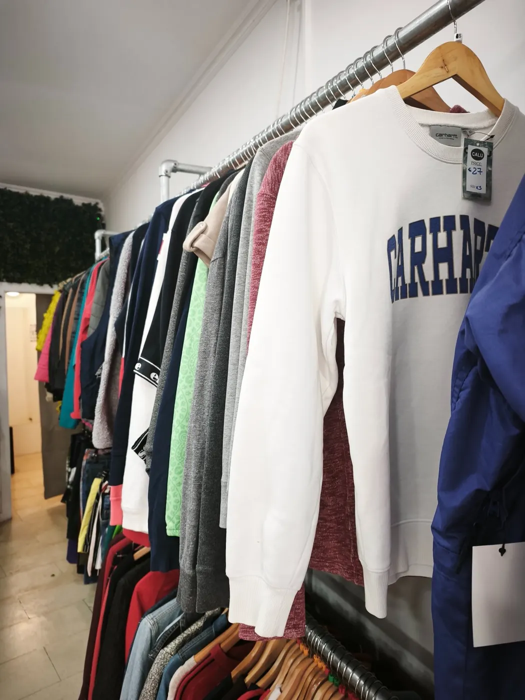 Sweatshirts e camisolas em segunda mão penduradas numa arara da CALU Porto